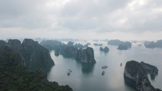 An array of small tropical islands with high cliffs and jungle on top. Boats sail between them.