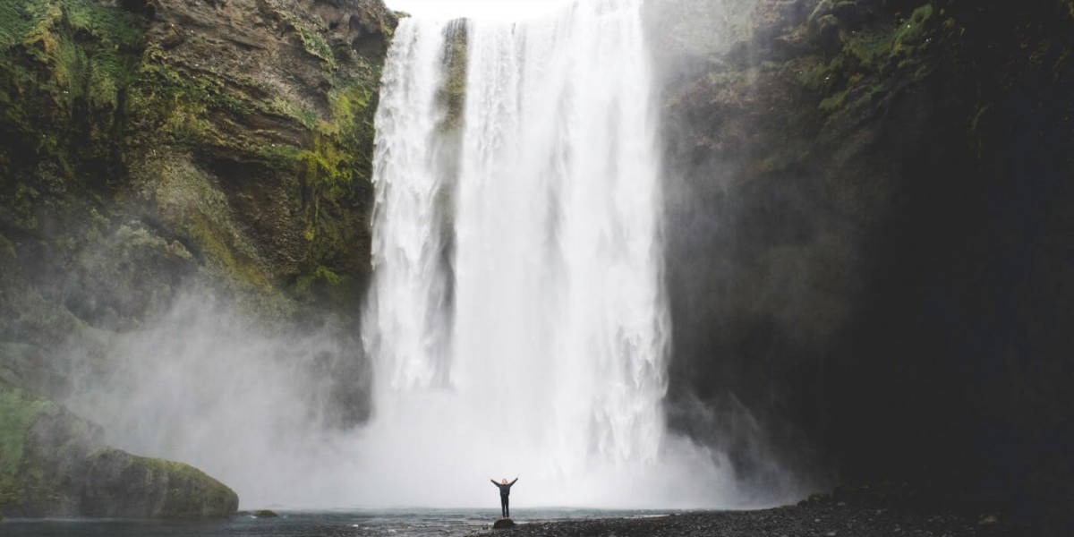 A huge waterfall in the background and a small figure standing at the bottom, raising their arms.